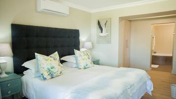 A bedroom with a large bed, two bedside tables with lamps, a wall-mounted air conditioner, and a door leading to a bathroom.