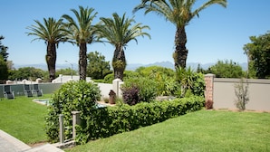A well-maintained garden with palm trees, a swimming pool, and a brick wall. - Four Palms Accommodation (Cape Town)