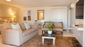 A living room with a sofa, chairs, a coffee table, and a TV. There is a desk with a chair and a lamp. - Four Palms Accommodation (Cape Town)