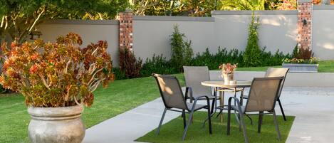 Une terrasse extérieure avec une table et des chaises, entourée d’une pelouse bien entretenue et d’un mur en briques.