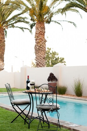 A poolside setting with a table and chairs, a bottle of wine, and a glass of wine. - Four Palms Accommodation (Cape Town)