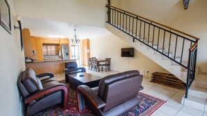 Een ruime woonkamer met een zithoek, een eettafel en een trap naar een bovenverdieping.