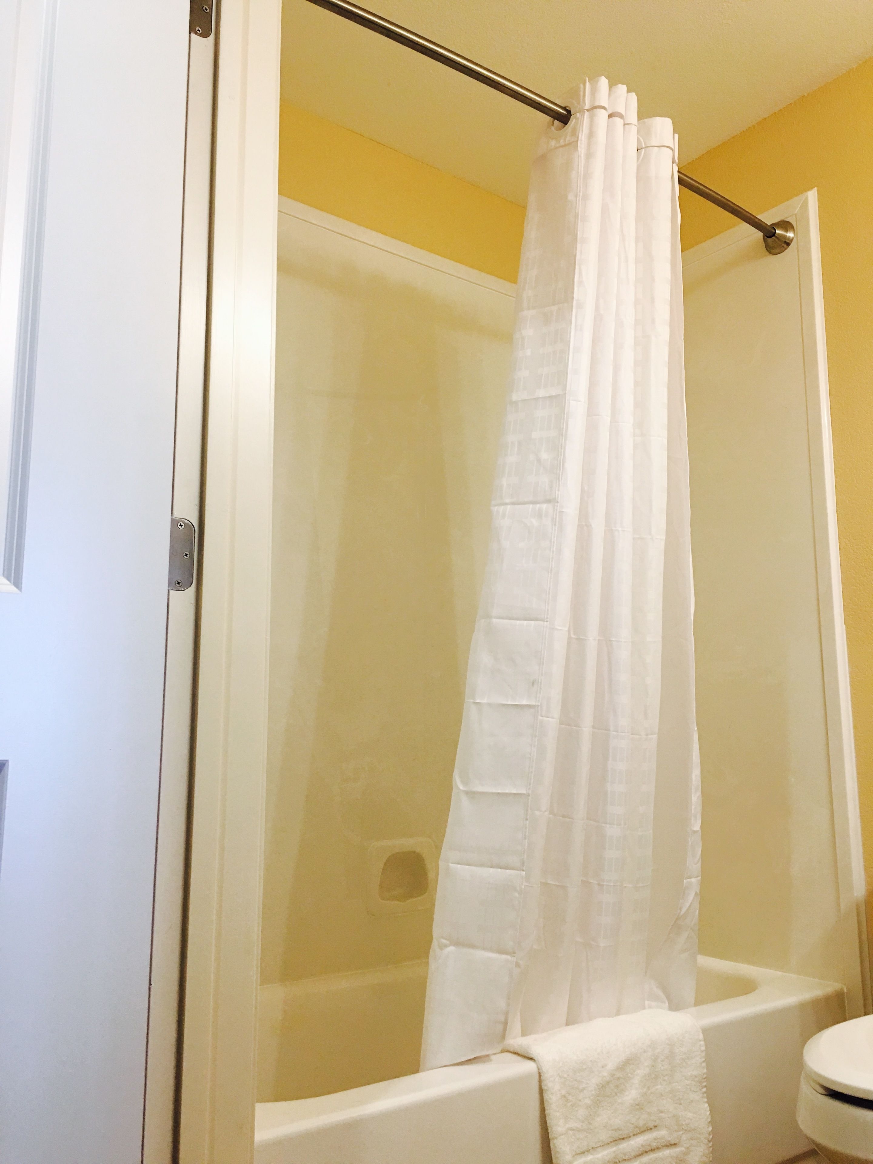 Un box de ducha con puerta de cristal, una cortina de ducha blanca y una bañera.