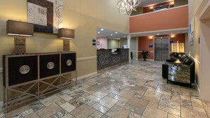 A lobby with a reception desk, a seating area, and a staircase leading to an upper level. - Days Inn & Suites by Wyndham Florence/Jackson Area (Florence)