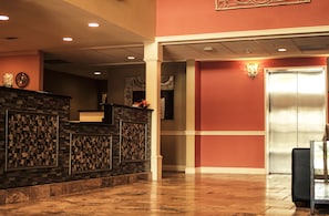 A reception area with a stone wall, a reception desk, a wall-mounted clock, and an elevator. - Days Inn & Suites by Wyndham Florence/Jackson Area (Florence)