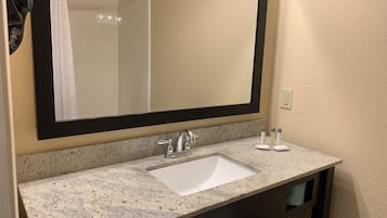 Uma casa de banho com bancada de granito, lavatório branco, espelho grande e um porta-toalhas.