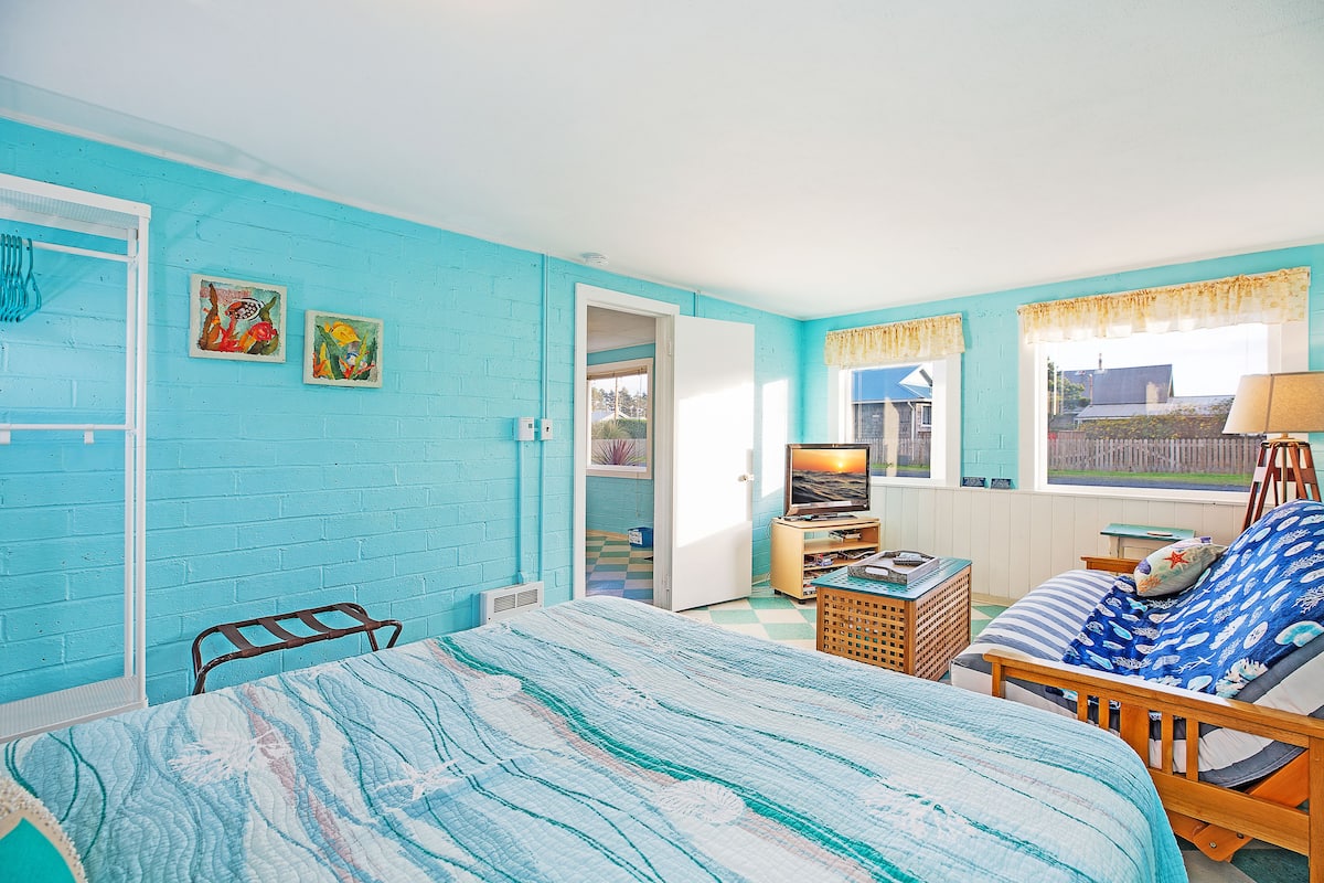 A room with a bed, a chair, a television, and artwork on the wall.