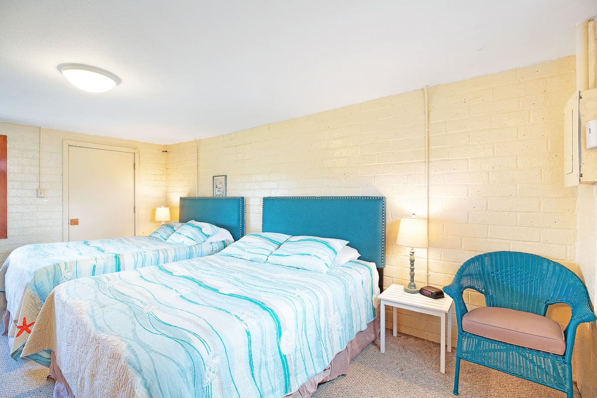 A hotel room with two beds, a chair, a nightstand, and a lamp.