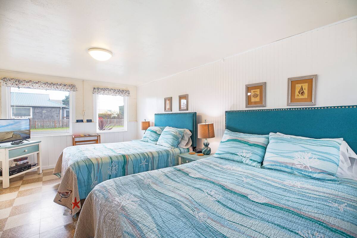 A bedroom with two beds, a television, and a window with a view of a building outside.