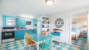 A kitchen with teal cabinets, a white stove, and a checkered floor. There is a dining table with chairs and a bookshelf. - Sand Dollar Condos (Pacific Beach)