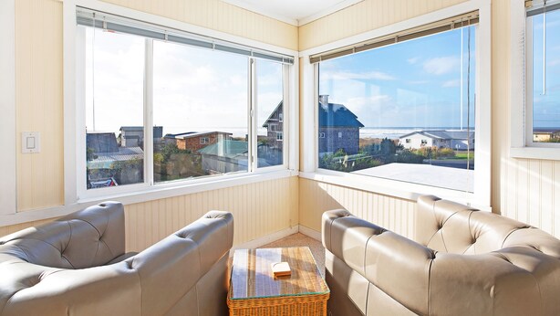 A corner room with two leather sofas, a small table, and large windows offering a view of houses and the sea. - Sand Dollar Condos (Pacific Beach)