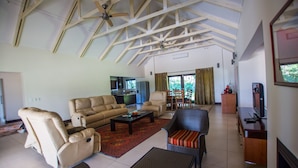A spacious living room with a high ceiling, a dining area, and a kitchen visible through an open door.