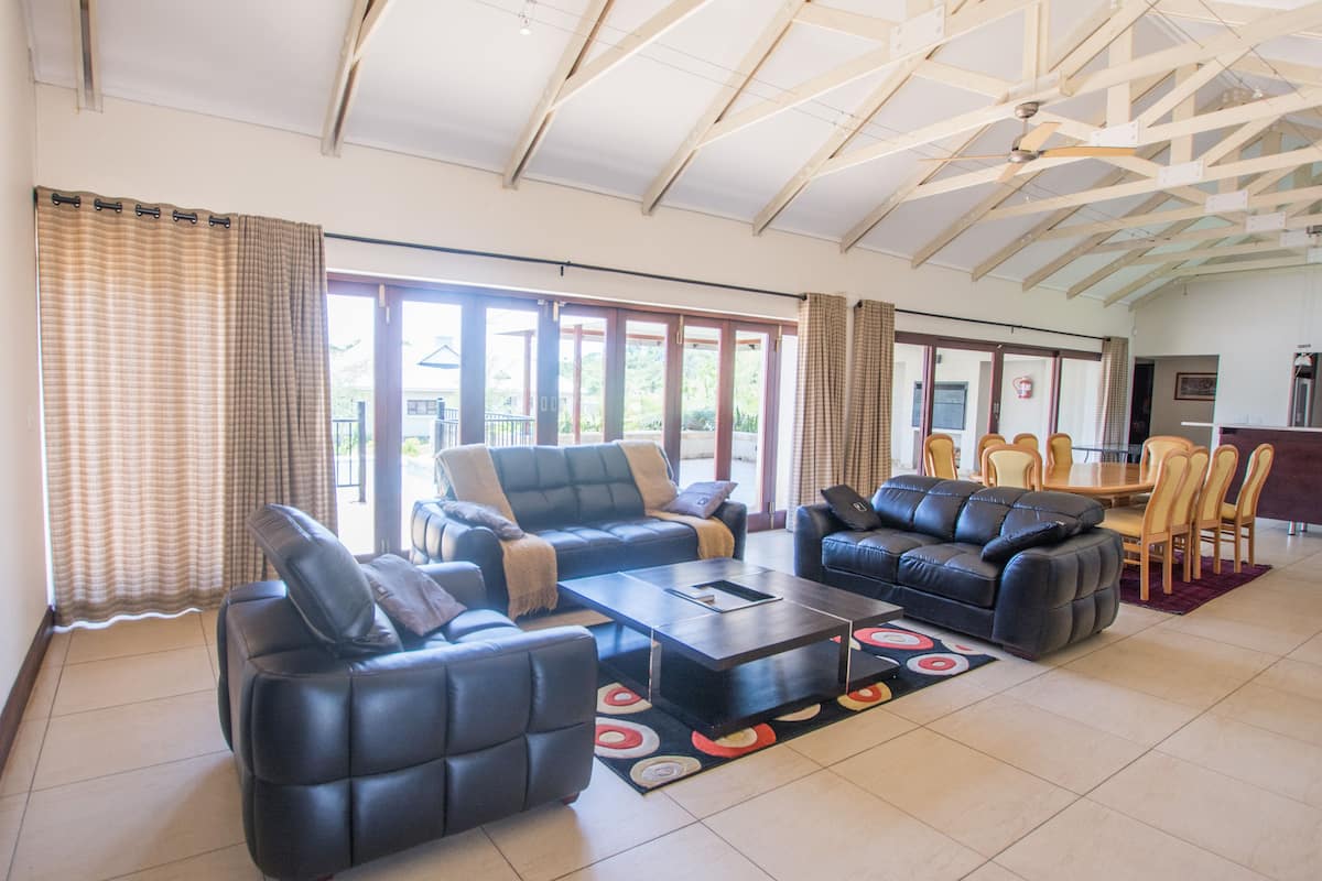 A spacious living room with a high ceiling, large windows, and a dining area with wooden furniture.