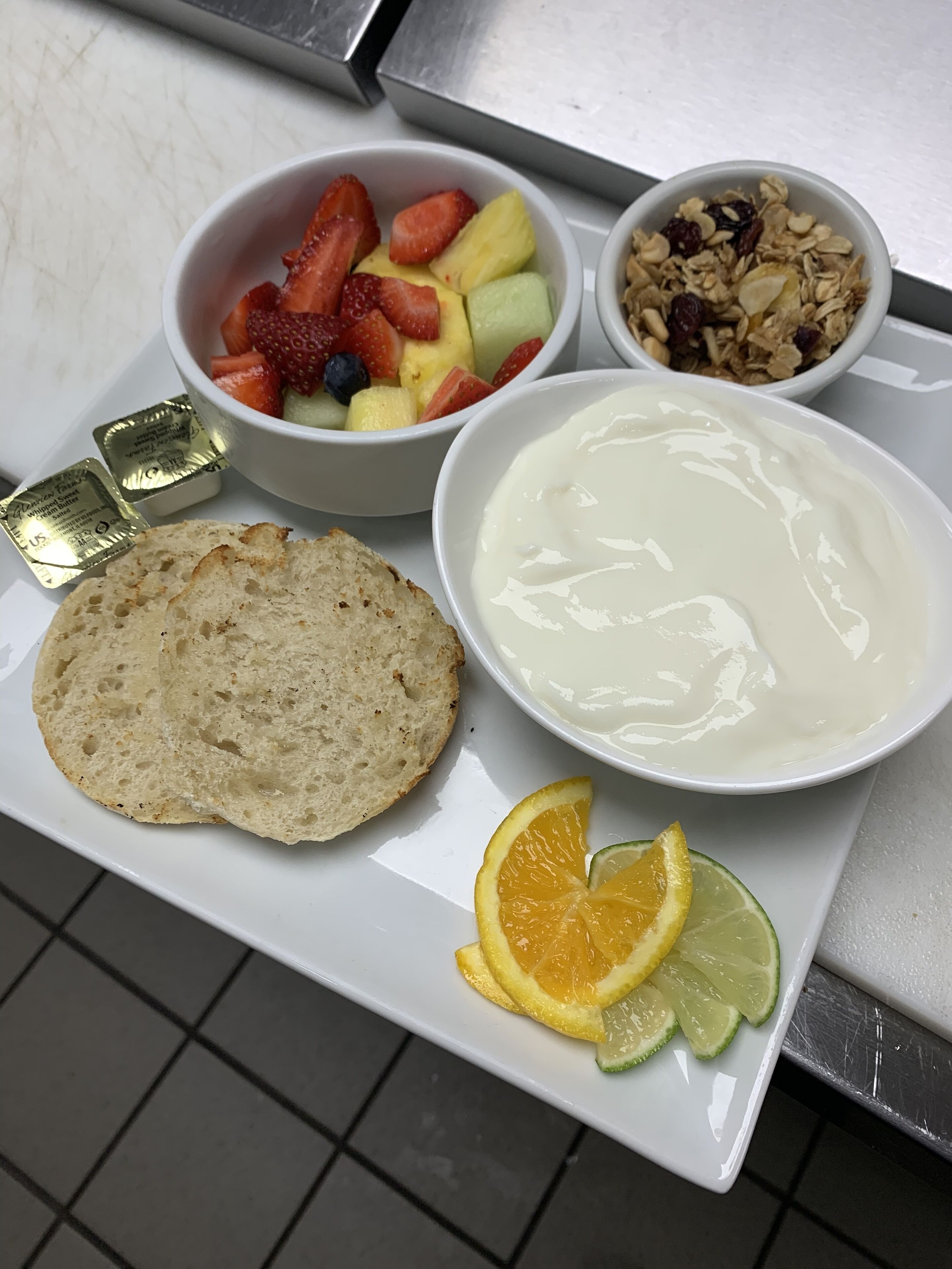 A breakfast tray with toast, yogurt, fruit, granola, and butter.