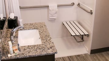 Ein modernes Badezimmer mit einem Waschtisch aus Granit, einem Spiegel, einem Handtuchhalter und einer Duschkabine mit Haltegriffen.