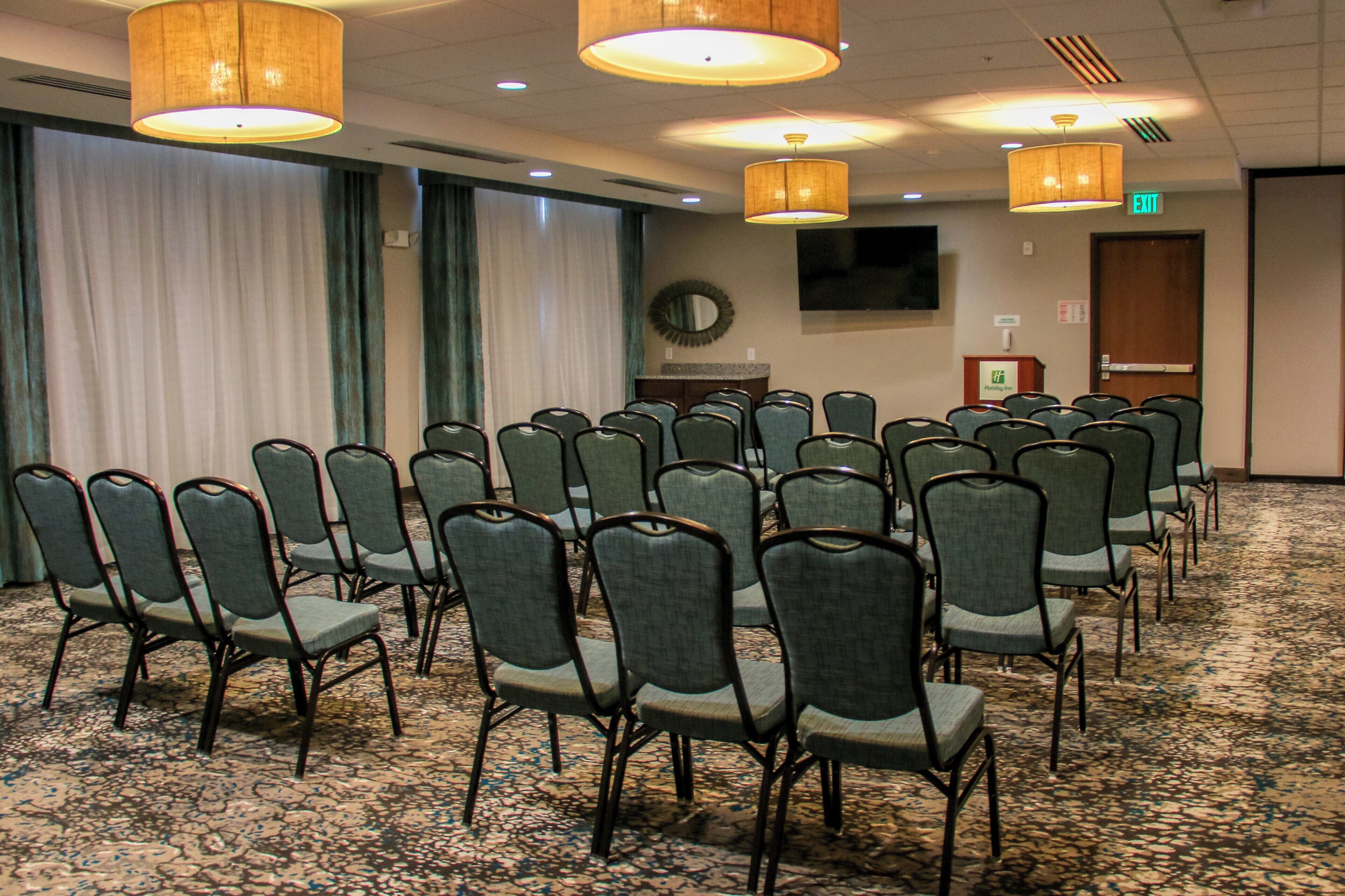 A conference room with rows of chairs, a podium, and a television screen on the wall.