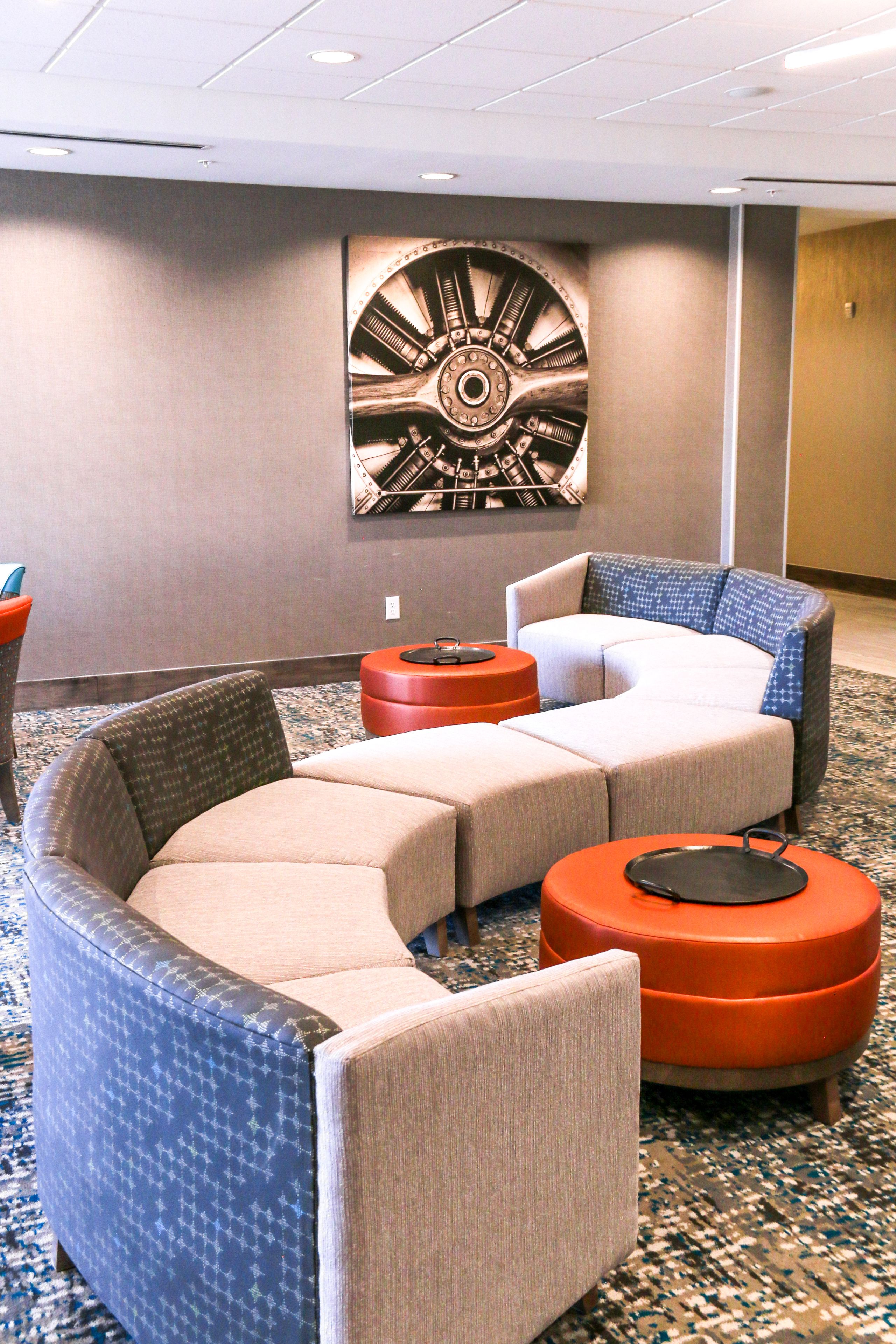 Un hall d’hôtel avec un canapé d’angle aux lignes courbes, un pouf rond orange et une grande œuvre d’art abstraite accrochée au mur.