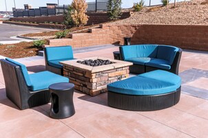 An outdoor seating area with a stone fire pit, cushioned chairs, and a small table.