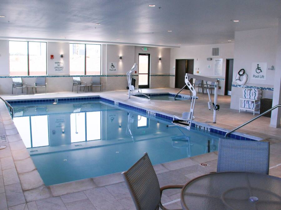 Una amplia piscina interior con varios elevadores de piscina, sillas y una mampara de vidrio.