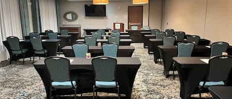 A conference room with multiple tables and chairs, a television on the wall, and a patterned carpet.