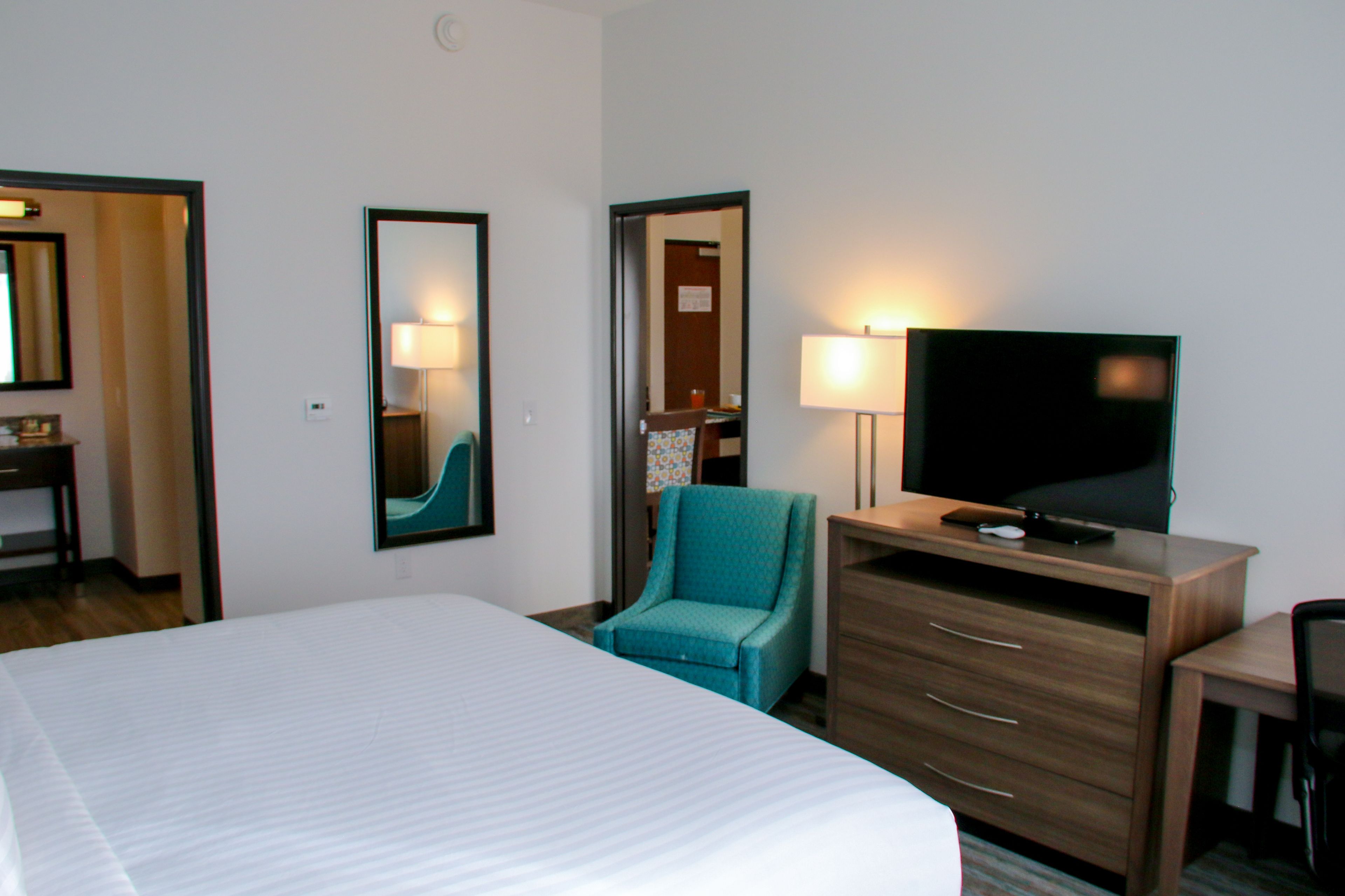Habitación de hotel con una cama grande, televisión, escritorio con cajones y una silla.