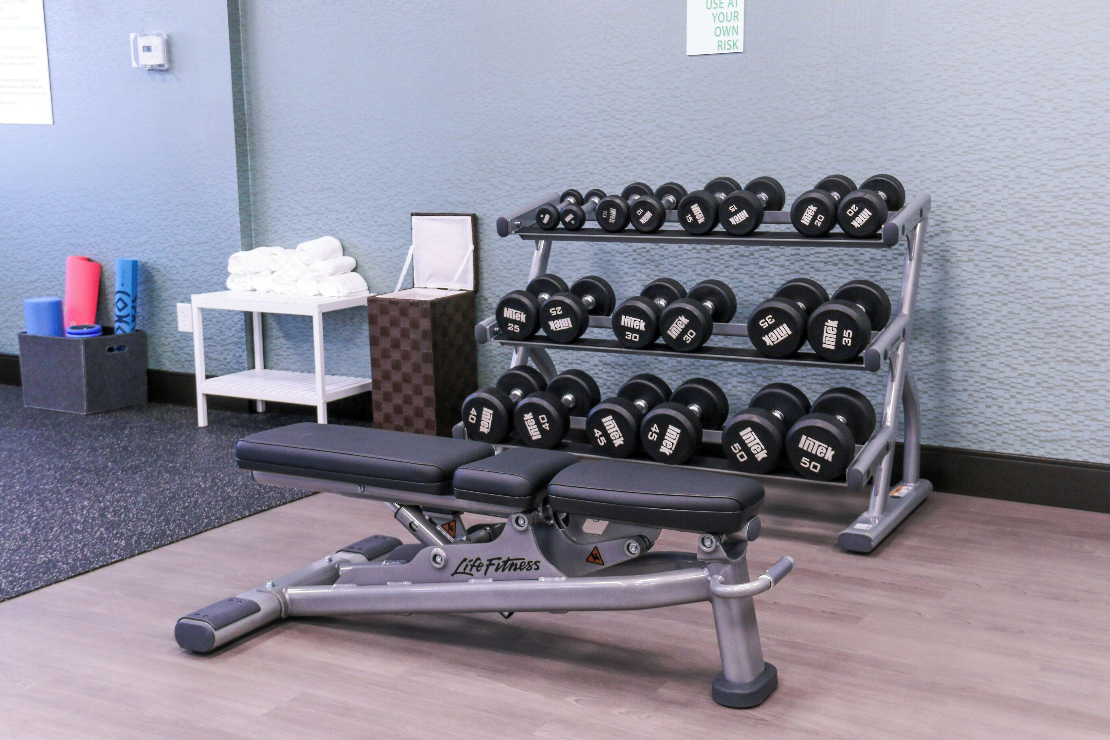 Un gimnasio con banco, mancuernas y un perchero para toallas.