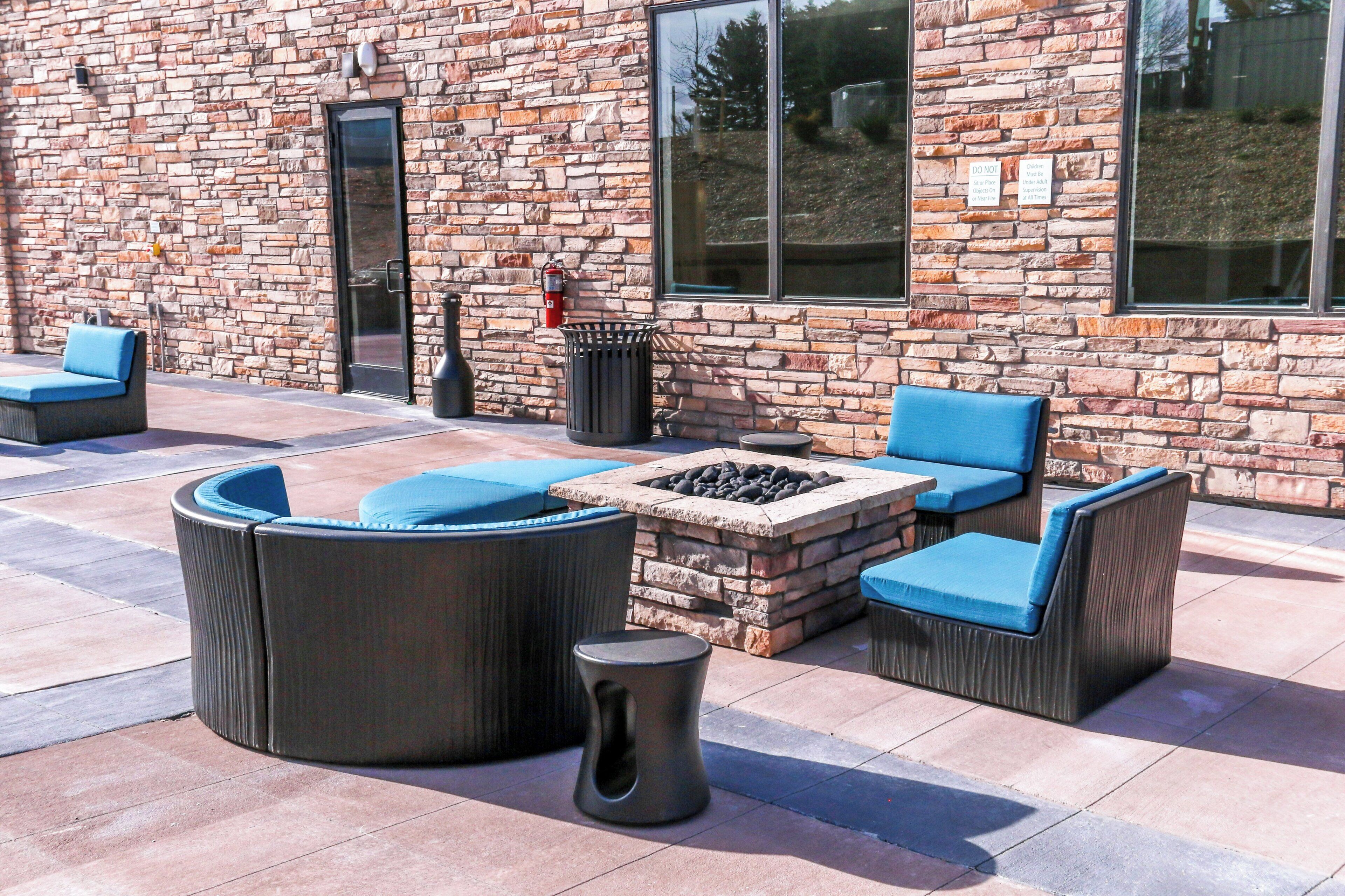 An outdoor seating area with a stone fire pit, cushioned chairs, and a trash can.