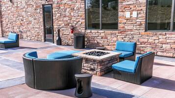 An outdoor seating area with a stone fire pit, cushioned chairs, and a trash can.