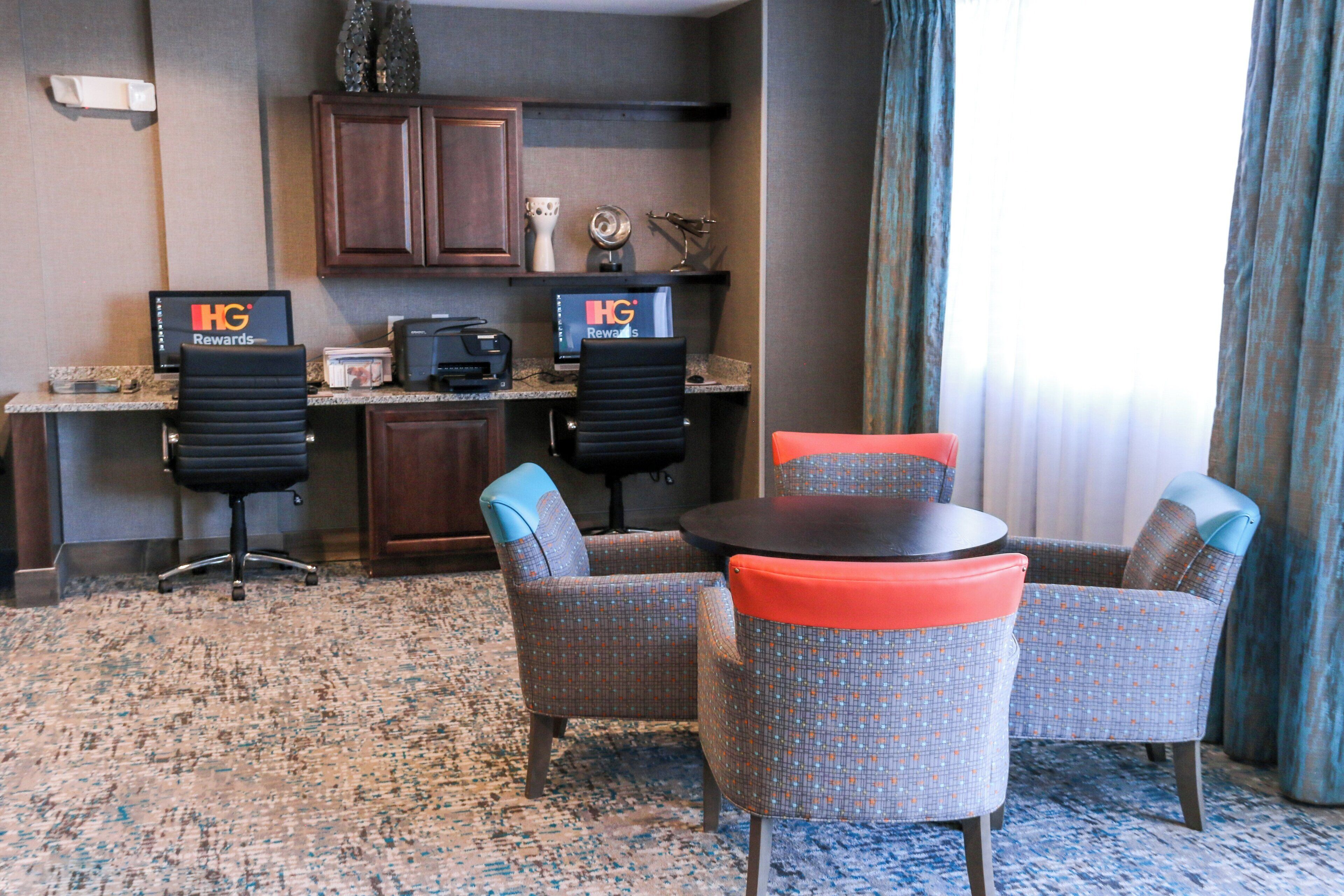A hotel room with a desk, two chairs, a small table, and a carpeted floor.
