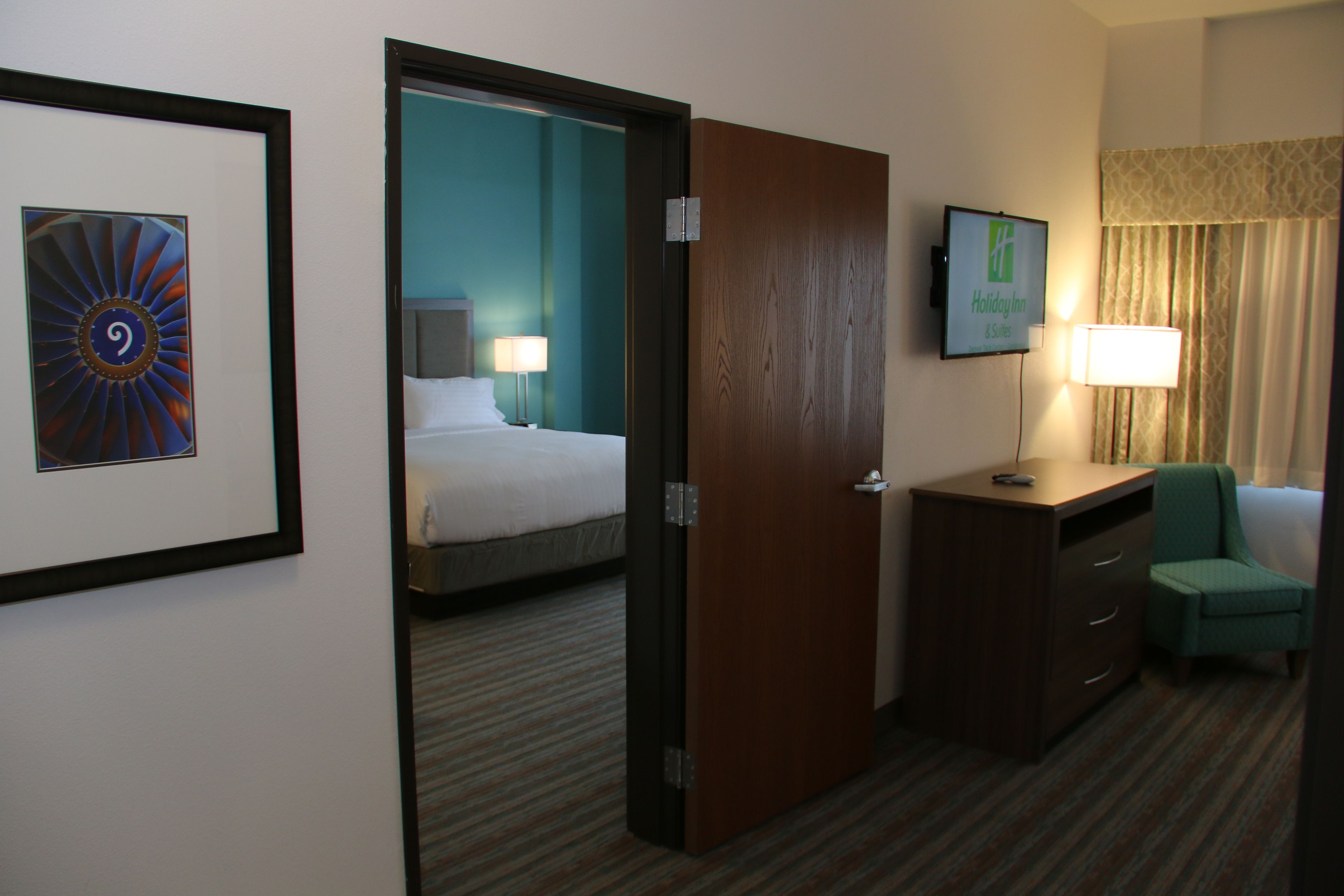 A hotel room with a bed, a desk, a chair, a TV, and a framed picture on the wall.