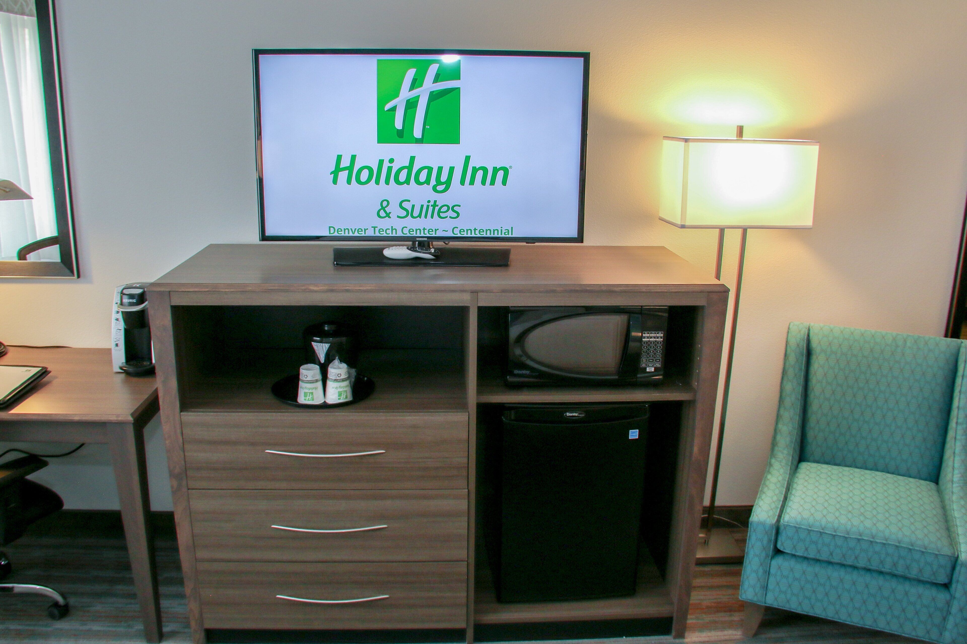 Habitación de hotel con cartel de Holiday Inn, un escritorio con lámpara, un microondas y una silla.