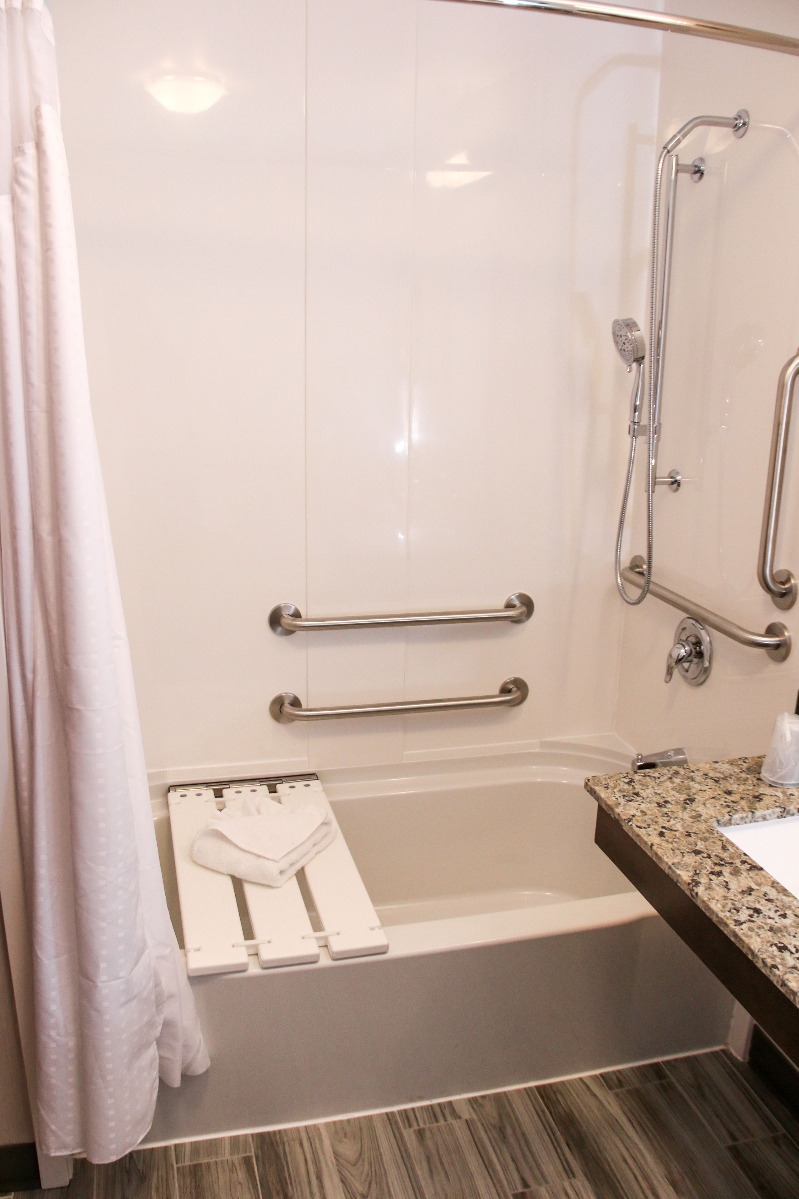 Un baño con ducha, barras de apoyo, toallero y lavamanos.