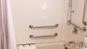 Un baño con ducha, barras de apoyo, toallero y lavamanos.