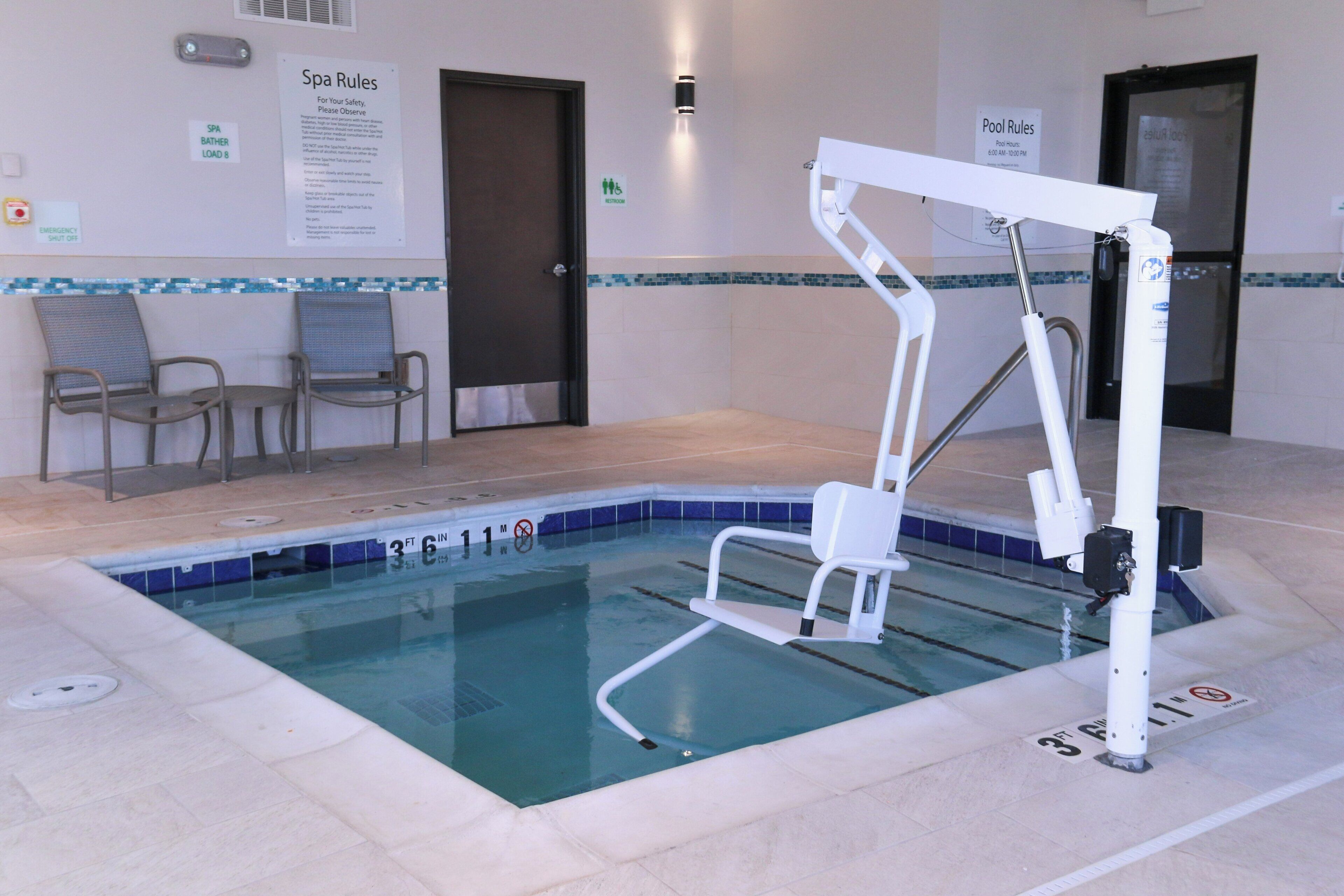A pool area with a lift chair, a sign indicating pool rules, and a sign for the spa rules.