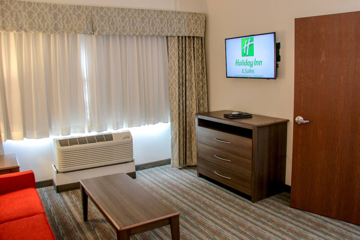 A hotel room with a bed, a desk, a chair, a TV on the wall, and a window with curtains.