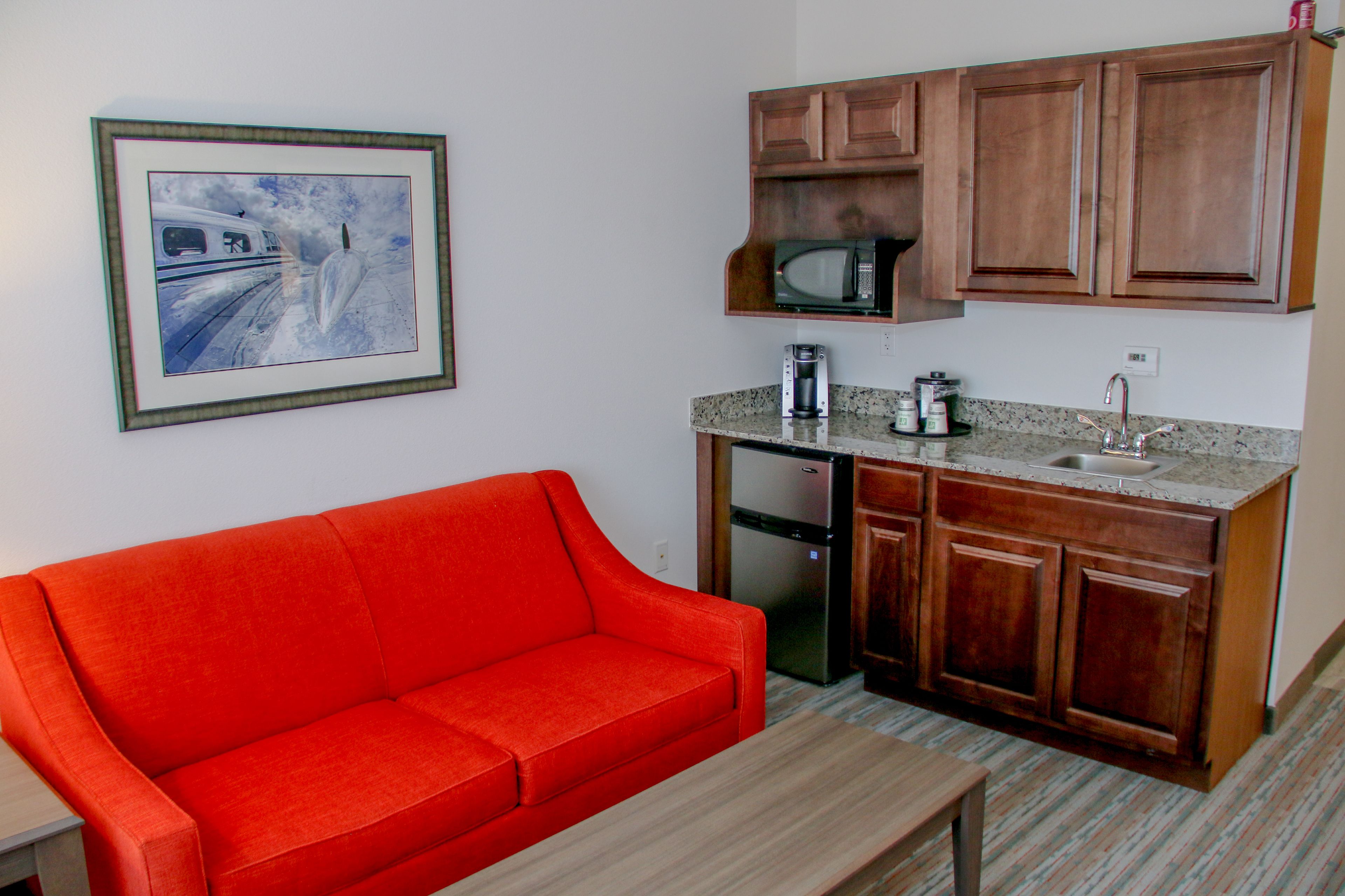 A compact living space with a kitchenette, a red sofa, a small table, and a framed picture on the wall.