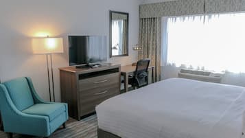 A hotel room with a bed, a desk, a chair, a television, a lamp, and a large window with curtains.