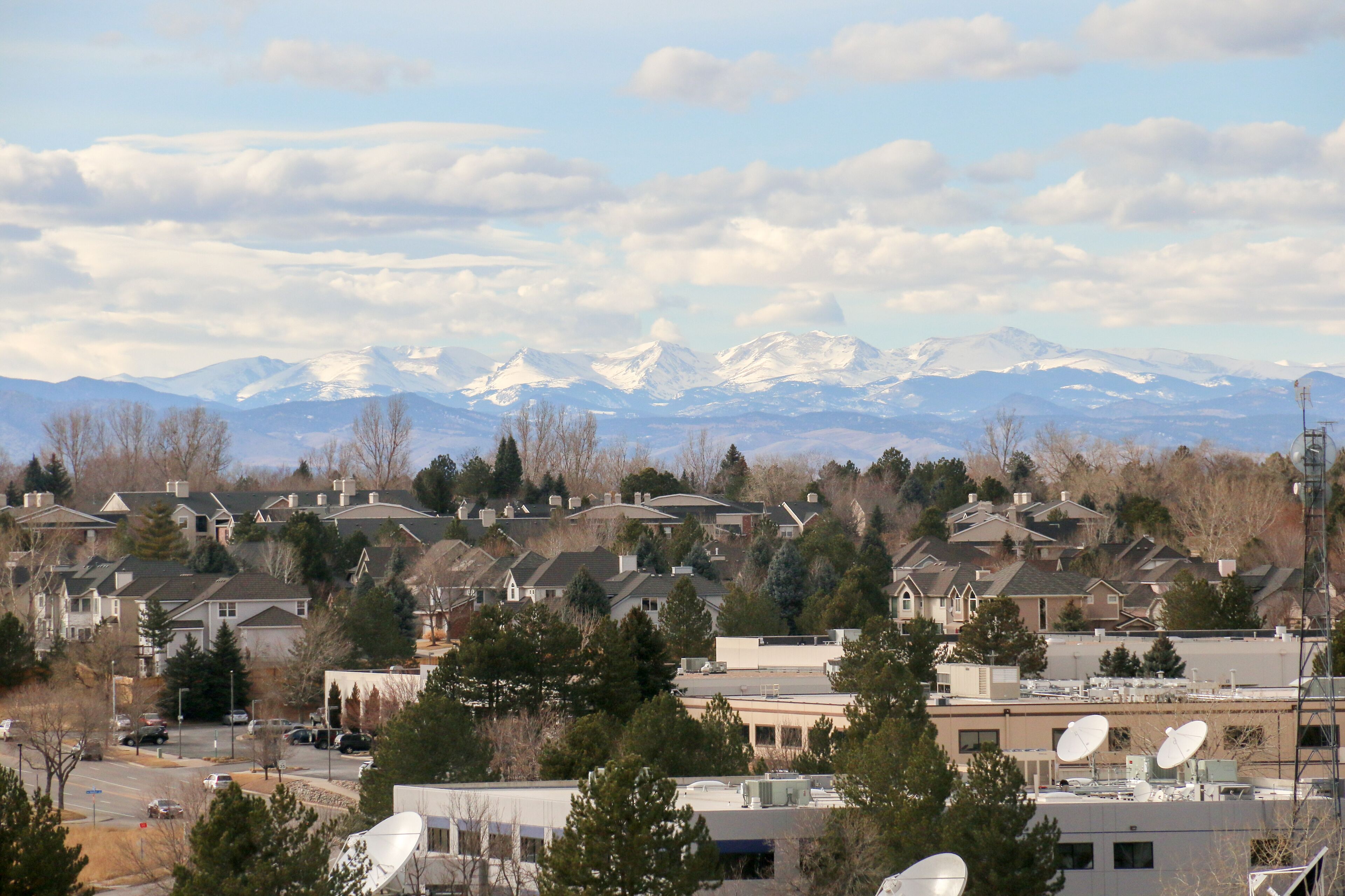 Un quartier résidentiel avec des maisons, des arbres et, au loin, une chaîne de montagnes.