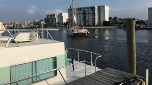 Un puerto deportivo con un velero amarrado, un muelle de madera y un paisaje urbano con edificios modernos al fondo.