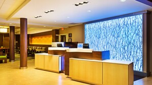 Een hotel receptie met houten balies, een groot digitaal scherm met een boompatroon, en een zithoek met tafels en stoelen.