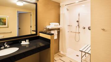 Un baño moderno con lavamanos de encimera negra, un espejo grande, ducha con puerta de vidrio y una mesita con toallas.