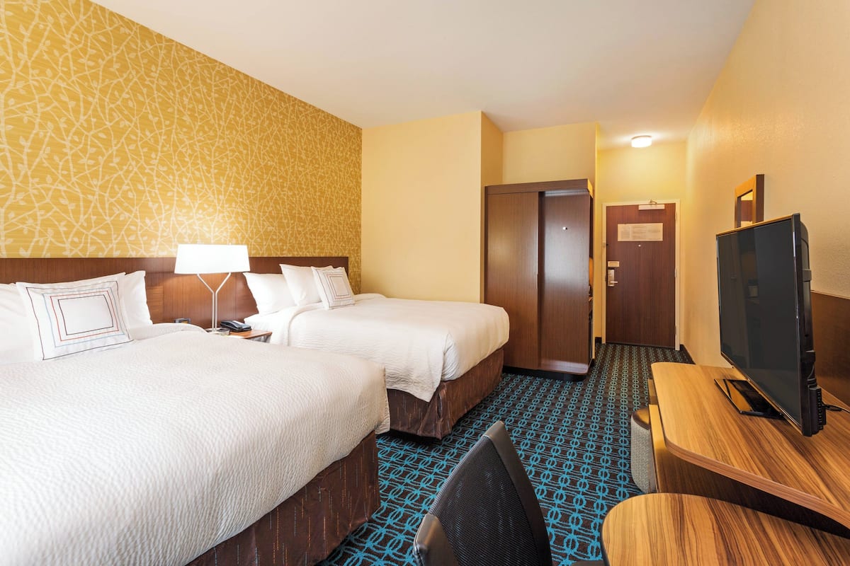 Habitación de hotel con dos camas, un escritorio, un televisor y una alfombra estampada.