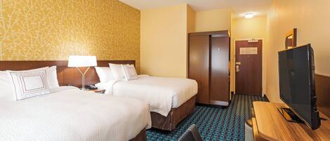 Habitación de hotel con dos camas, un escritorio, un televisor y una alfombra estampada.
