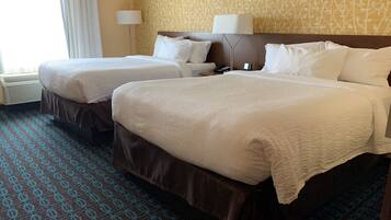 A hotel room with two beds, a patterned carpet, a wall with a branch design, and a lamp.