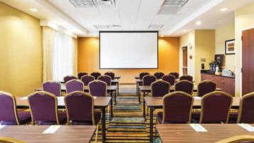 A conference room with rows of tables and chairs, a large projection screen, and a kitchenette area.