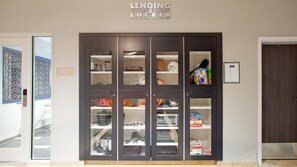 A LENDING LOCKER with multiple compartments, including shelves for books, games, and kitchenware. - Candlewood Suites Kearney by IHG (Kearney)