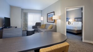 Une chambre d’hôtel comprenant une table à manger aux lignes courbes, un canapé, un fauteuil, un téléviseur, une lampe et un lit.