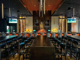 Un área de bar con una barra larga, distintos arreglos de asientos y un diseño de techo moderno.