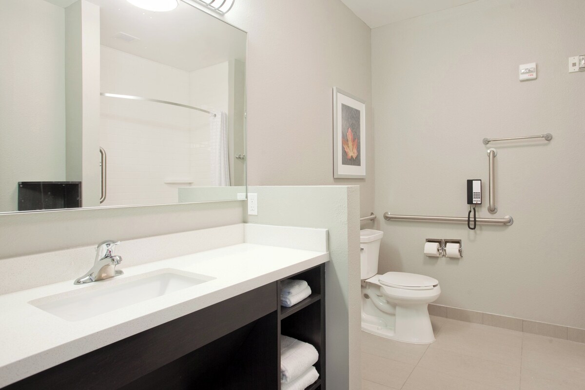 A modern bathroom with a white sink, toilet, and shower. There are handrails and a telephone mounted on the wall.