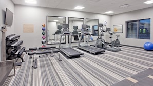 Une salle de sport équipée de tapis de course, de vélos elliptiques et de poids libres.